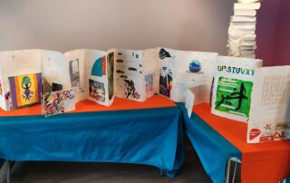 Photographie en couleurs : une table accueille le livre d'artiste fait par les patients et patientes, c'est un livre-accordéon ou leporello où l'on voit des dessins colorés et des textes