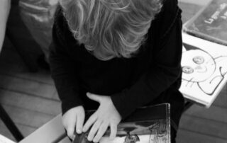 Photographie en noir et blanc. Un jeune enfant est penché sur un livre illustré.