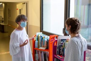 Les lectrices de Livre Passerelle au service de néonatologie de l’hôpital de Tours © Marie Pétry Deux femmes vêtues de blouses, le visage recouvert d'un masque antigénique, discutent devant deux chariots remplis de livres jeunesse